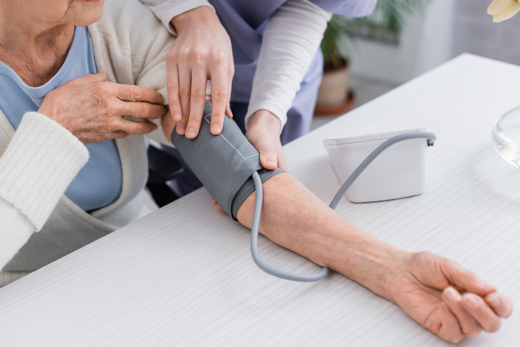 oříznutý pohled na sociální pracovnici měřící krevní tlak seniorky s tonometrem - Fotografie, Obrázek