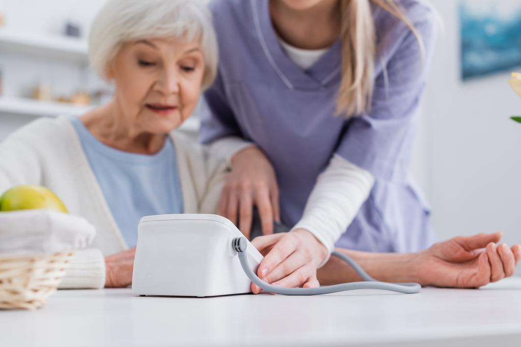 selektiver Fokus des Tonometers in der Nähe von älterer Frau und Krankenschwester auf verschwommenem Hintergrund - Foto, Bild