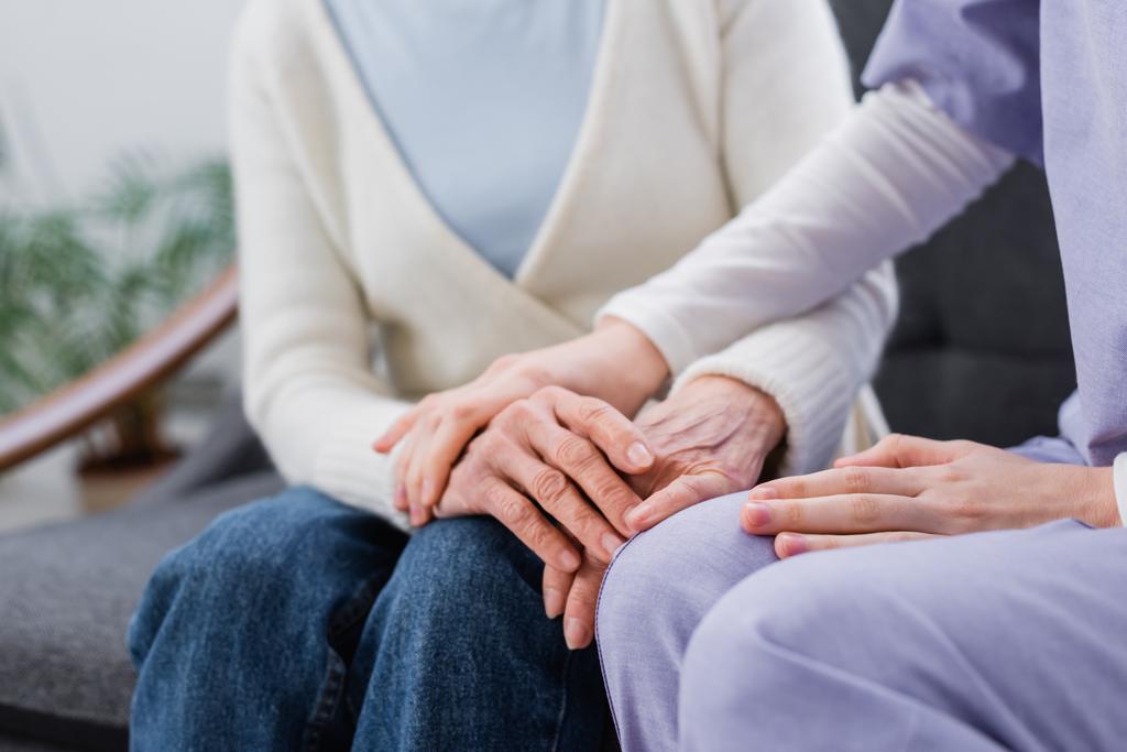 ořezaný pohled na ošetřovatelku dotýkající se ruky starší ženy doma - Fotografie, Obrázek