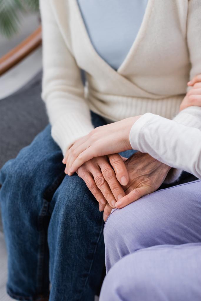 Hemşirenin yaşlı bir kadının yanında oturması ve eline dokunması, bulanık bir arka plan. - Fotoğraf, Görsel