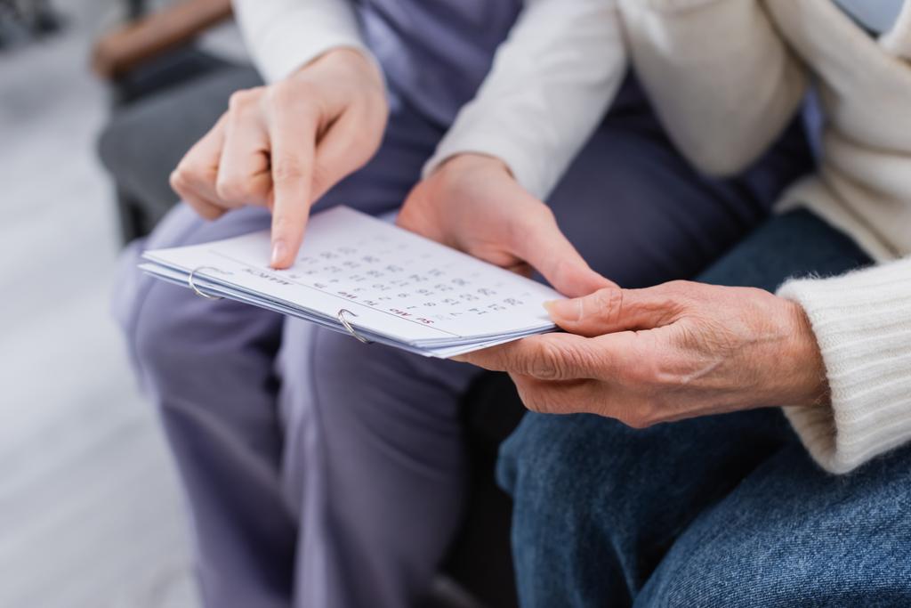 visão parcial da assistente social apontando calendário próximo a mulher idosa doente por amnésia - Foto, Imagem