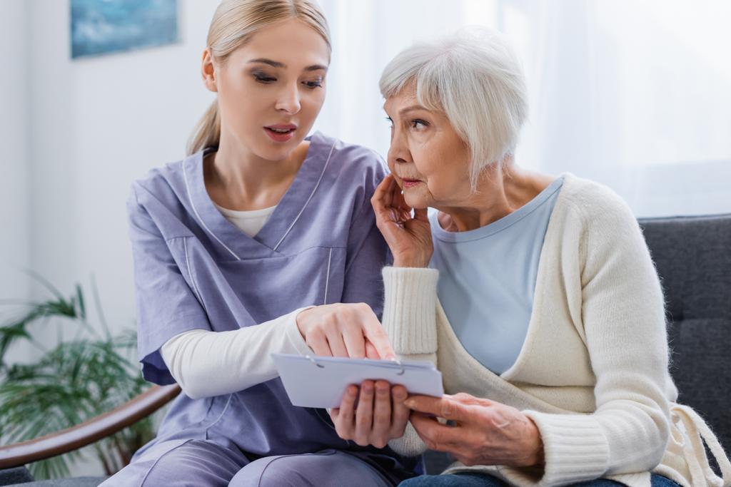 nuori sairaanhoitaja osoittaa kalenteriin lähellä iäkäs nainen sairas dementia - Valokuva, kuva