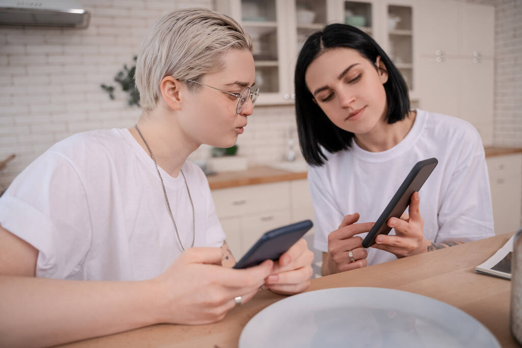 young lesbian couple using cellphones in kitchen  - Photo, Image