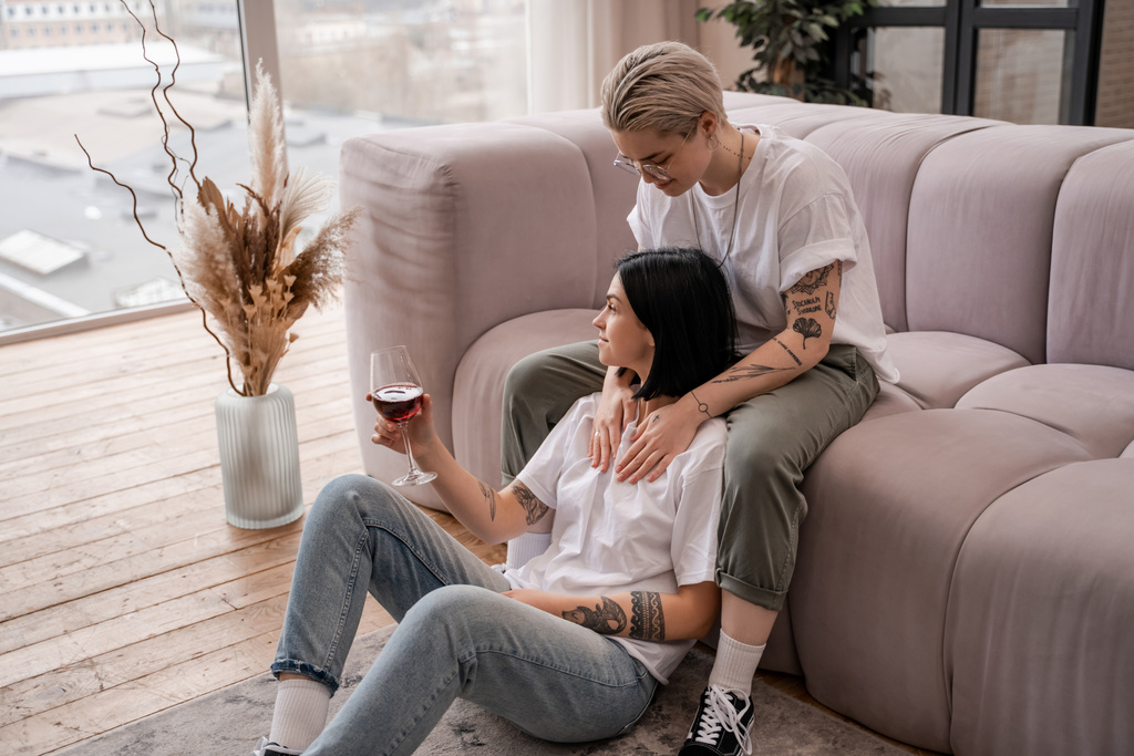 tattooed woman looking at happy girlfriend with glass of red wine  - Photo, Image