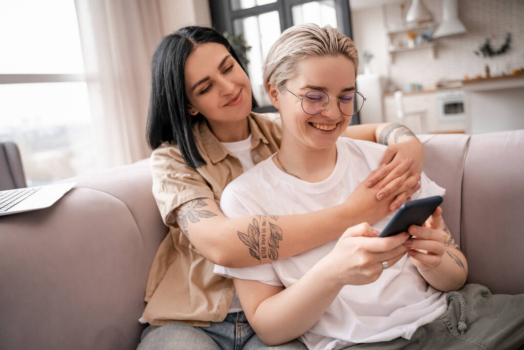 felice coppia lesbica guardando smartphone mentre si rilassa sul divano - Foto, immagini