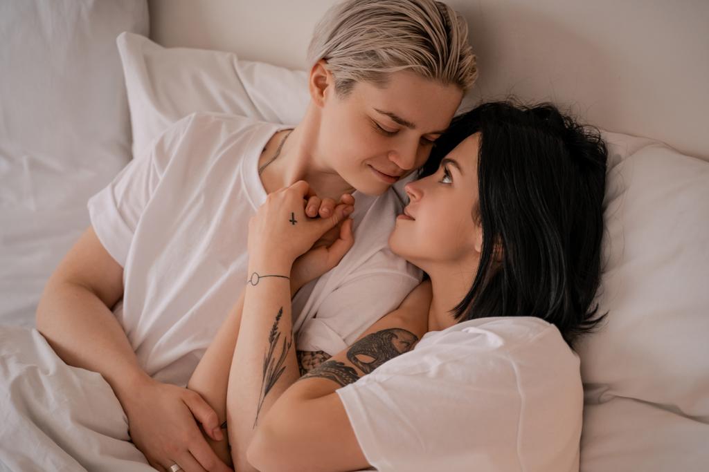 любляча молода лесбіянка пара лежить в ліжку і тримає руки
 - Фото, зображення
