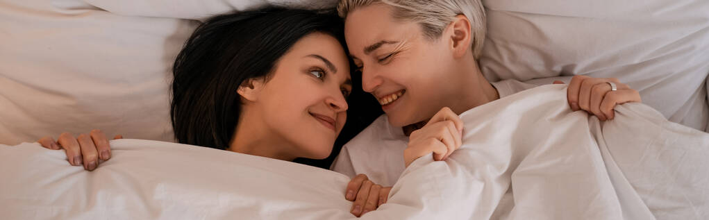 vista superior de la feliz pareja de lesbianas tumbados en la cama debajo de la manta, bandera - Foto, imagen