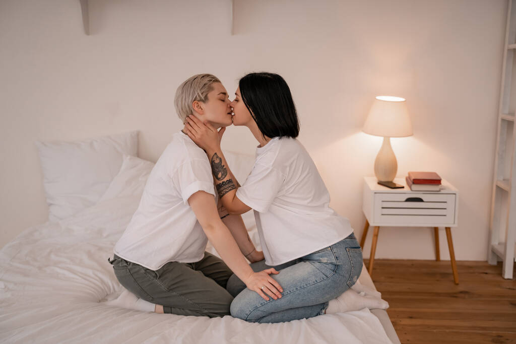 ベッドの上でキスしているレズビアンカップルの側面図 - 写真・画像