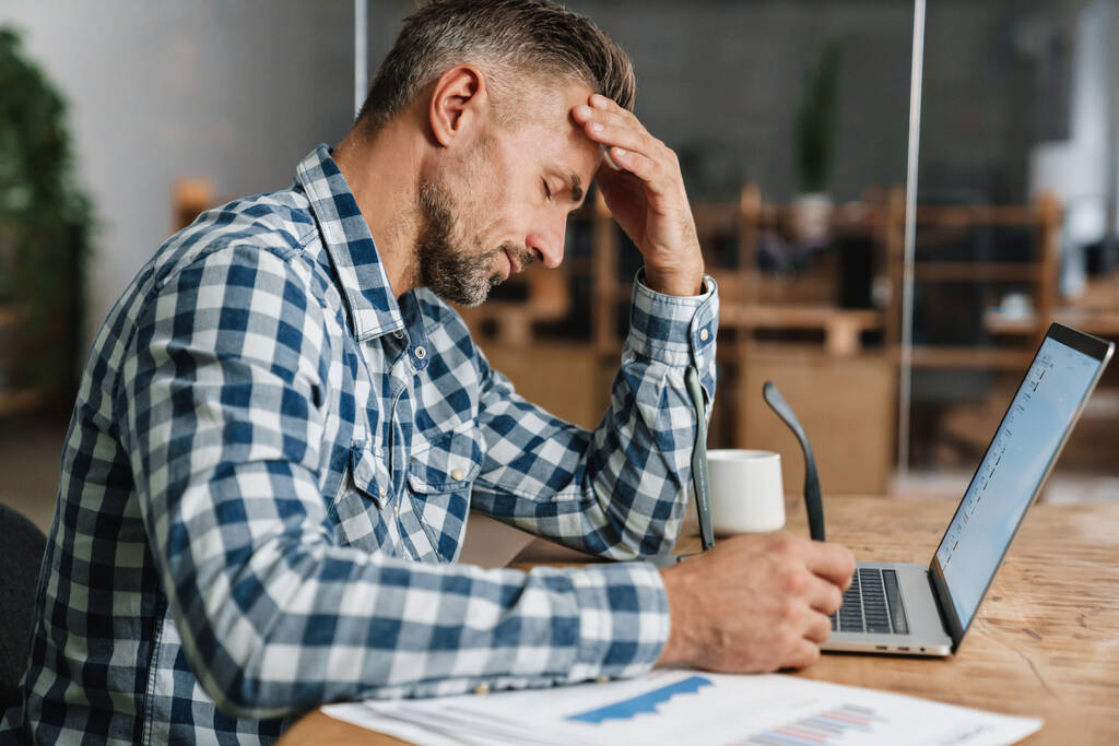 Hombre gris cansado que trabaja con el ordenador portátil mientras está sentado en la oficina - Foto, Imagen