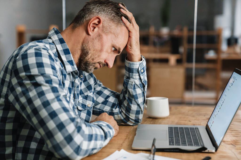 Unavený šedý muž pracuje s notebookem, zatímco sedí v kanceláři - Fotografie, Obrázek