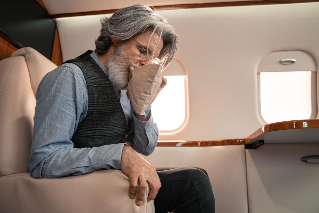 Mature man breathing in air sickness bag in private jet  - Photo, Image