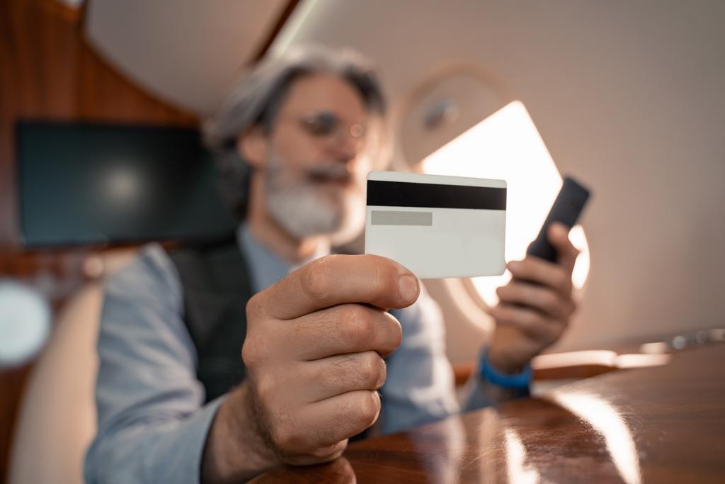 ジェットの背景にぼやけたスマートフォンを使用しているビジネスマンの手のクレジットカード  - 写真・画像
