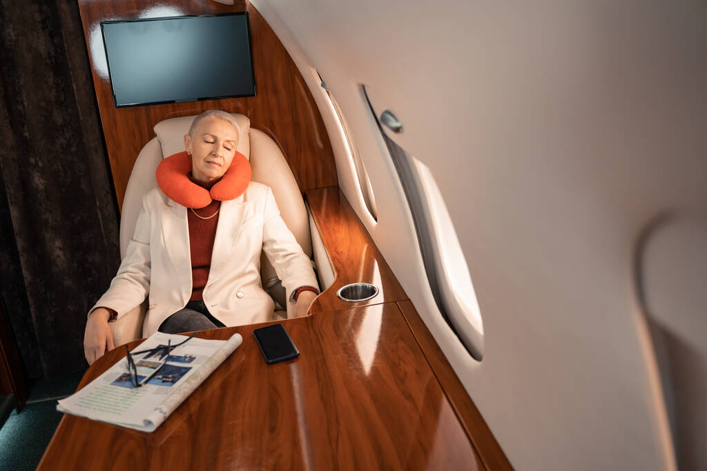 Zakenvrouw in de nek kussen slapen in de buurt van tijdschrift en smartphone in prive-jet  - Foto, afbeelding