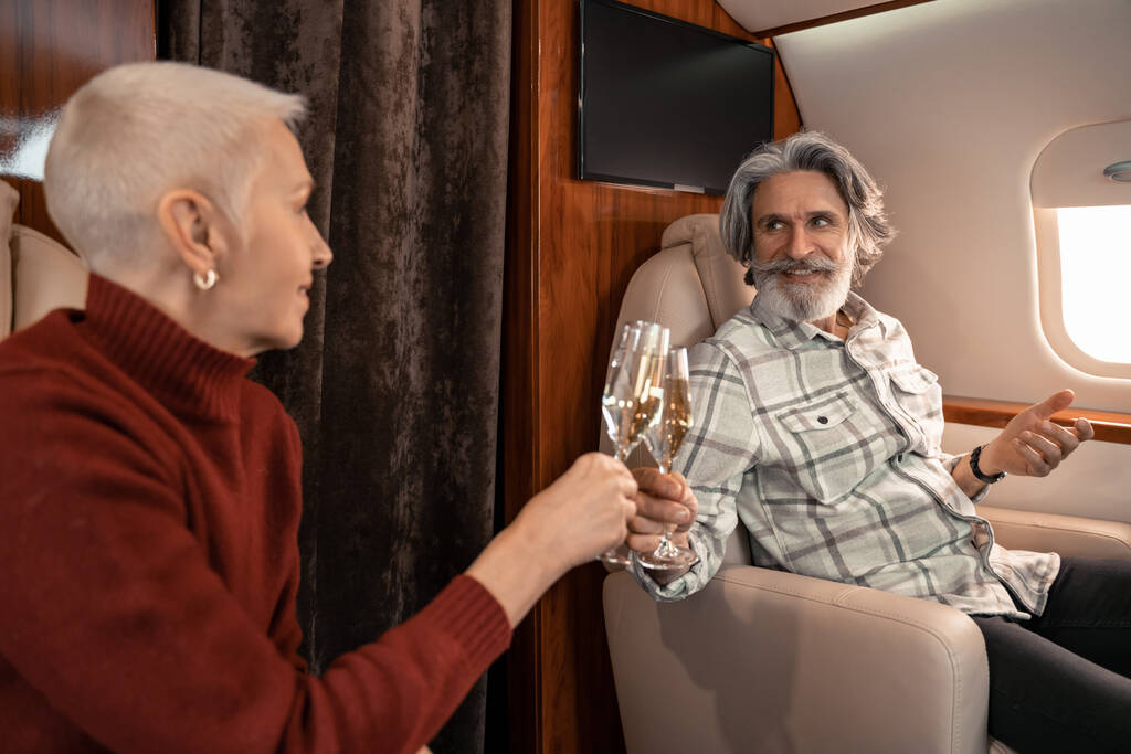 Mature man clinking champagne with mature wife on blurred foreground in jet - Photo, Image