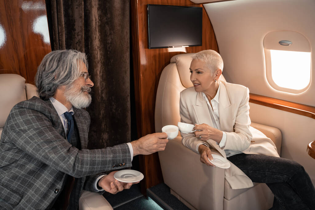 Cheerful business people clinking with coffee cups in private plane  - Photo, Image