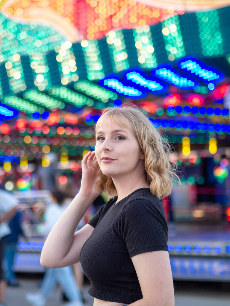 Eine vertikale Aufnahme einer blonden Frau mit einem Piercing posiert in einem Vergnügungspark - Foto, Bild