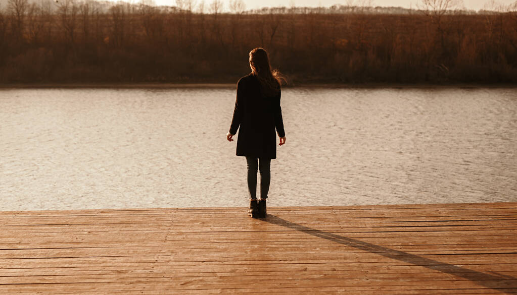 Frau in schwarzem Outfit steht auf Seebrücke am Fluss - Foto, Bild