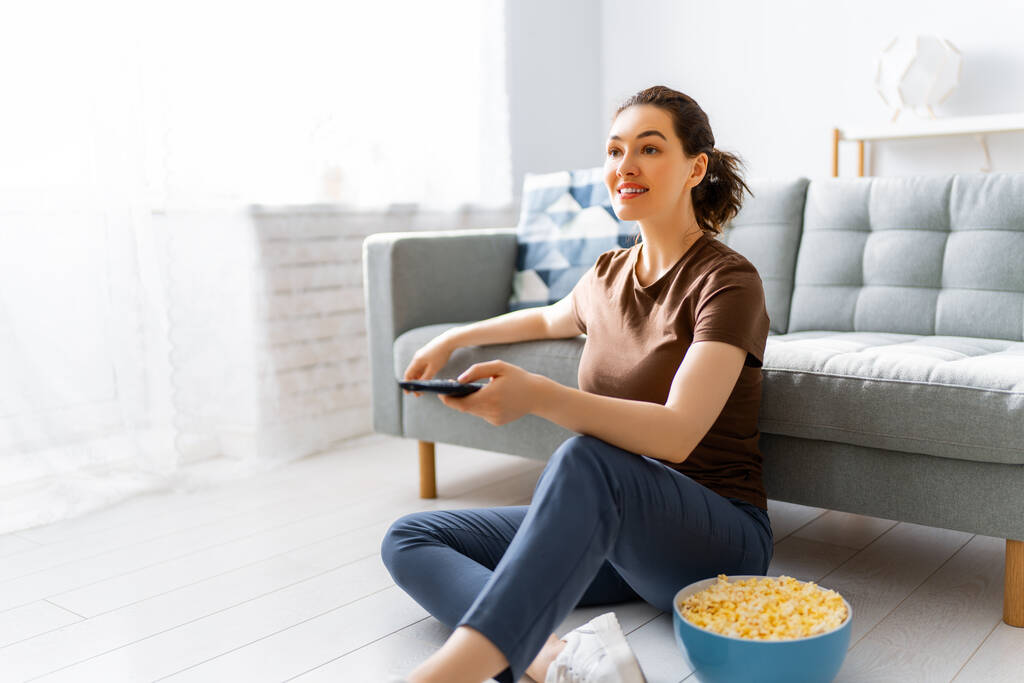Молодая женщина смотрит телевизор, фильмы с попкорном. Девочка проводит время дома. - Фото, изображение