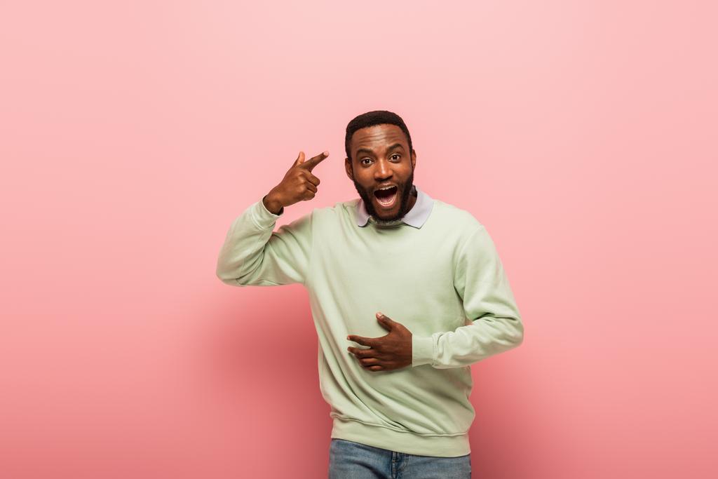 Ενθουσιασμένος Αφροαμερικάνος που δείχνει το κεφάλι του σε ροζ φόντο.  - Φωτογραφία, εικόνα