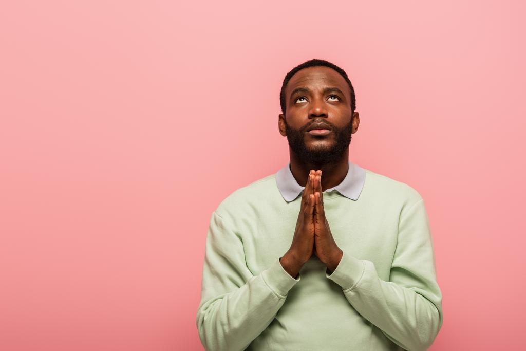 Dua eden elleri olan Afro-Amerikan bir adam pembe üzerine tek başına bakıyor.  - Fotoğraf, Görsel