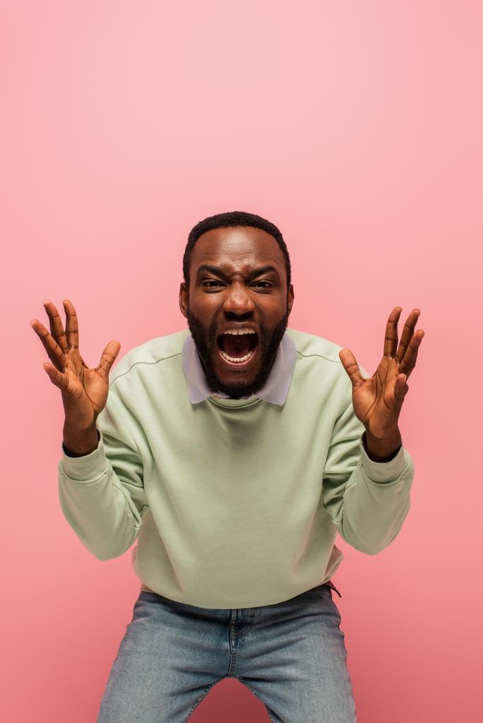 schreeuwende afrikaanse amerikaanse man op zoek naar camera op roze achtergrond  - Foto, afbeelding