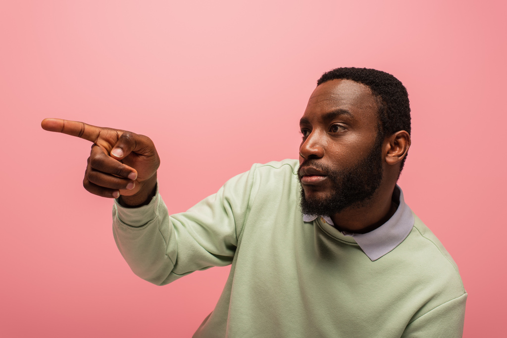 Africký Američan ukazuje prstem a dívá se stranou izolované na růžové  - Fotografie, Obrázek