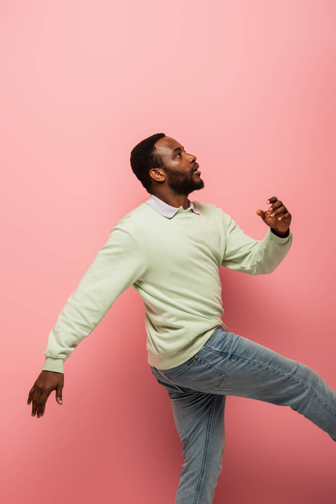 Seitenansicht von afrikanisch-amerikanischen Mann zu Fuß auf rosa Hintergrund  - Foto, Bild