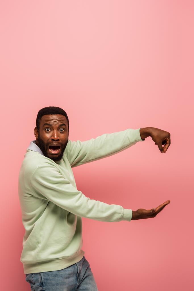 Φοβισμένος Αφροαμερικάνος που κρατάει κάτι απομονωμένο στο ροζ.  - Φωτογραφία, εικόνα