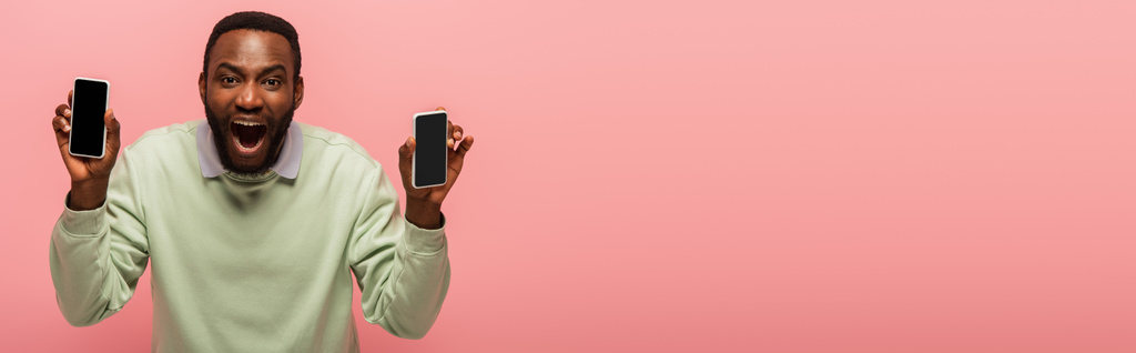 興奮したアフリカ系アメリカ人男性のスマートフォンはピンク、バナーに隔離された  - 写真・画像