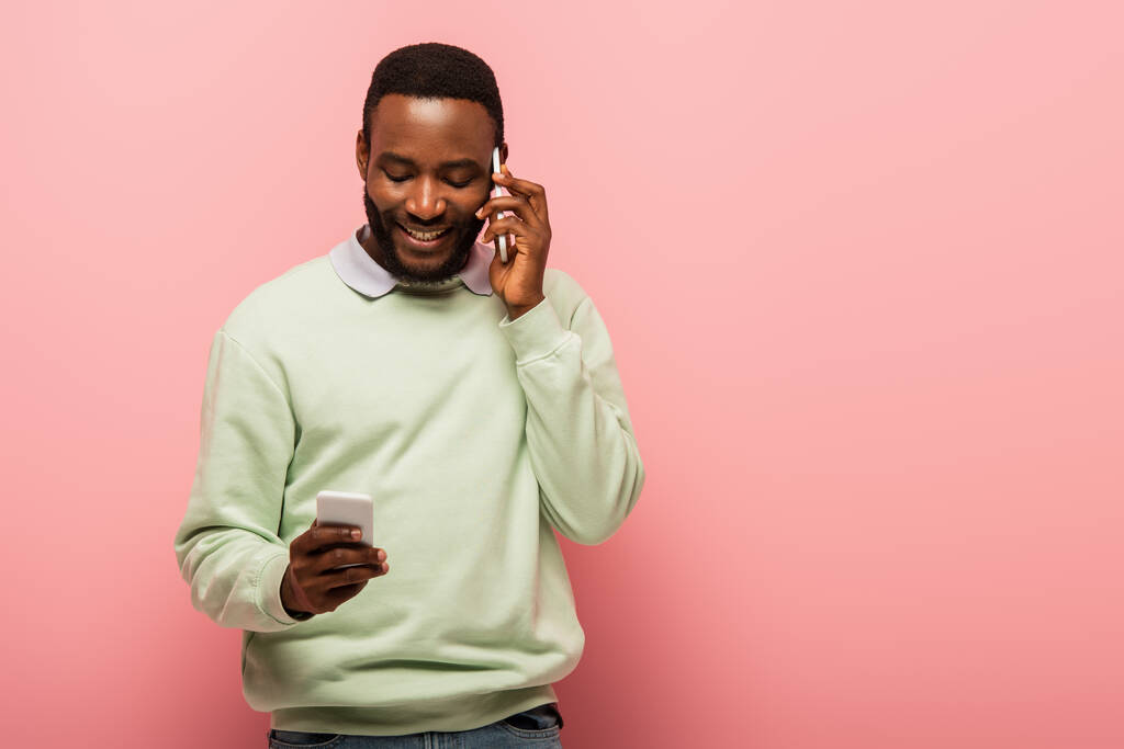 Jonge Afrikaanse Amerikaanse man praten en het gebruik van mobiele telefoon op roze achtergrond  - Foto, afbeelding