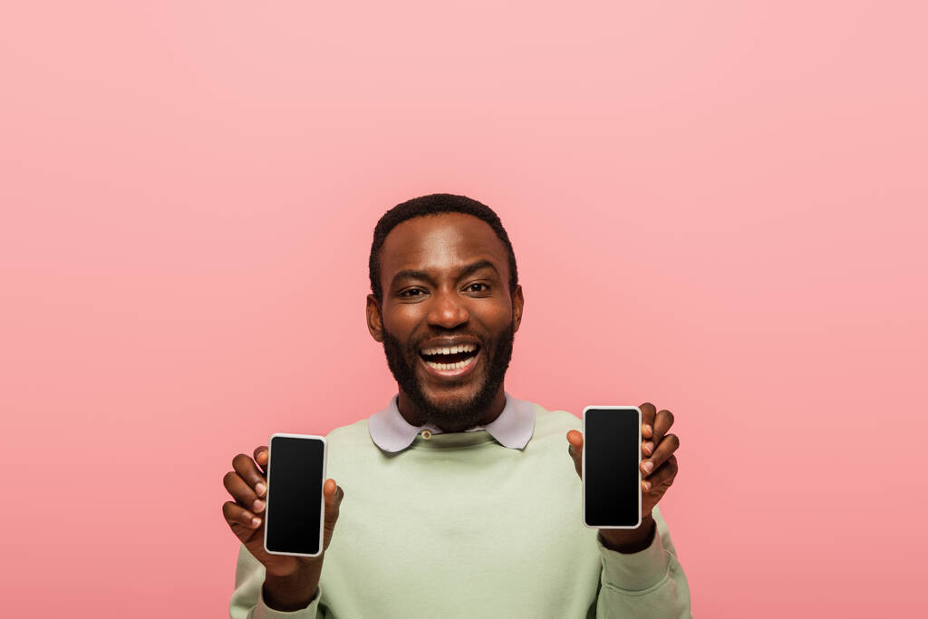 Веселый африканский американец с мобильными телефонами, изолированными на розовом  - Фото, изображение
