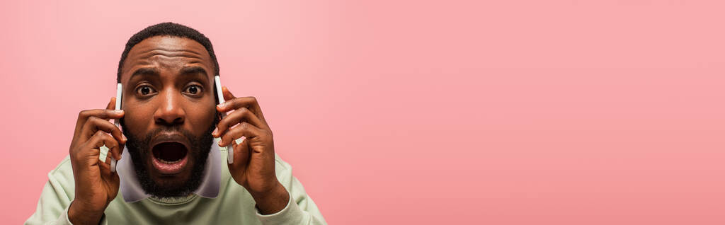 Приголомшений афроамериканець розмовляє на смартфонах ізольованих рожевим, з копіювальним простором, банером.  - Фото, зображення