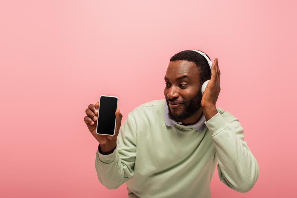 Uomo afroamericano utilizzando le cuffie e tenendo smartphone isolato su rosa  - Foto, immagini