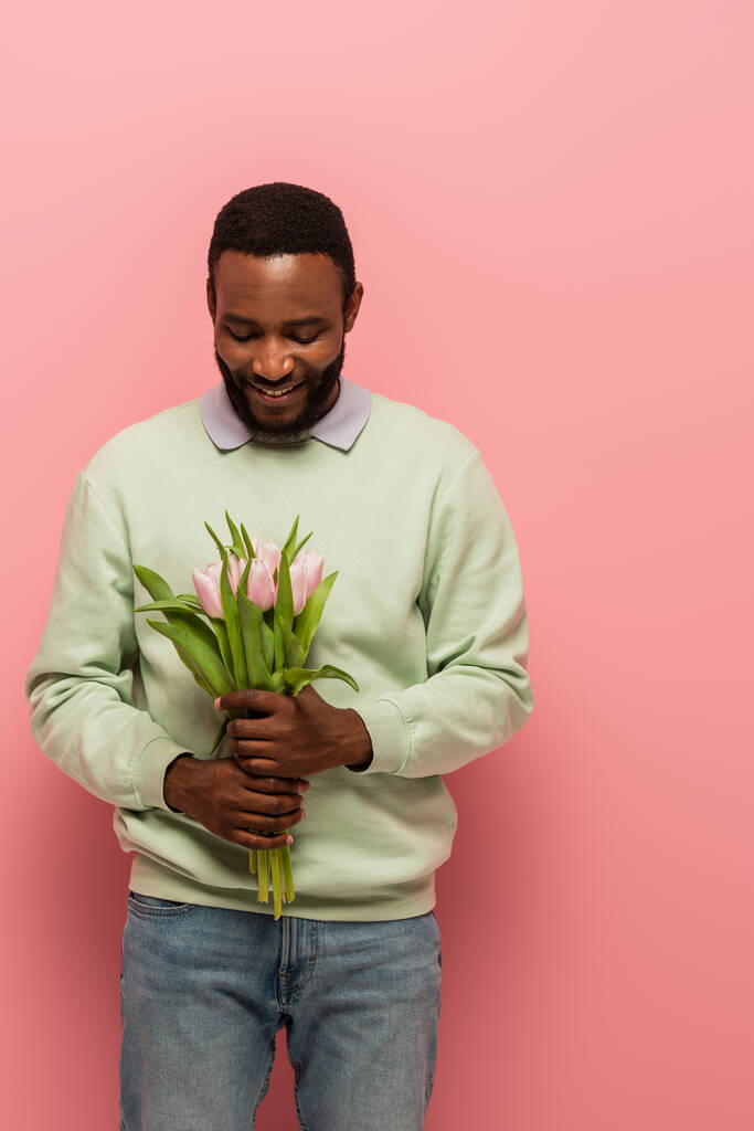 hombre afroamericano feliz celebración ramo de tulipanes sobre fondo rosa - Foto, Imagen