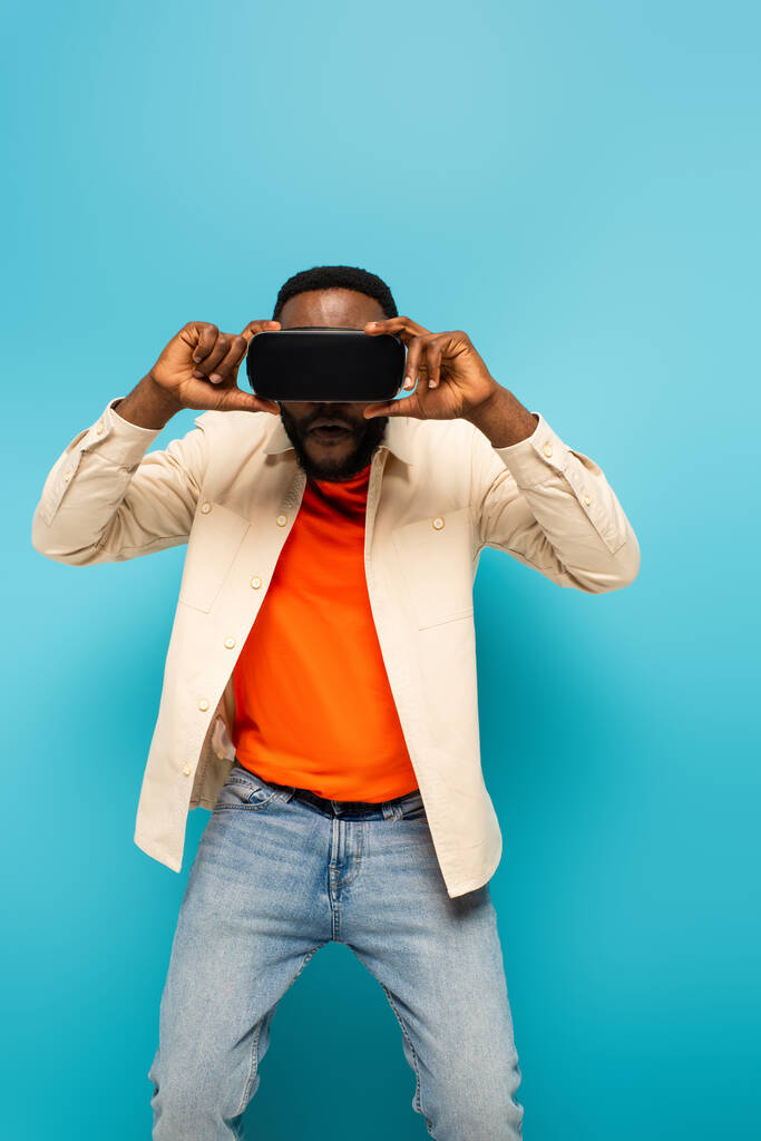 afrikanisch-amerikanischer Mann justiert vr-Headset auf blauem Hintergrund - Foto, Bild