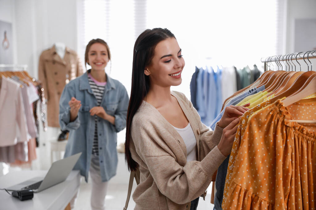 Assistante de magasin aidant le client à choisir des vêtements dans la boutique moderne - Photo, image