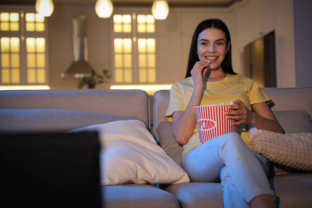 Young woman watching movie with popcorn on sofa at night, space for text - Photo, Image
