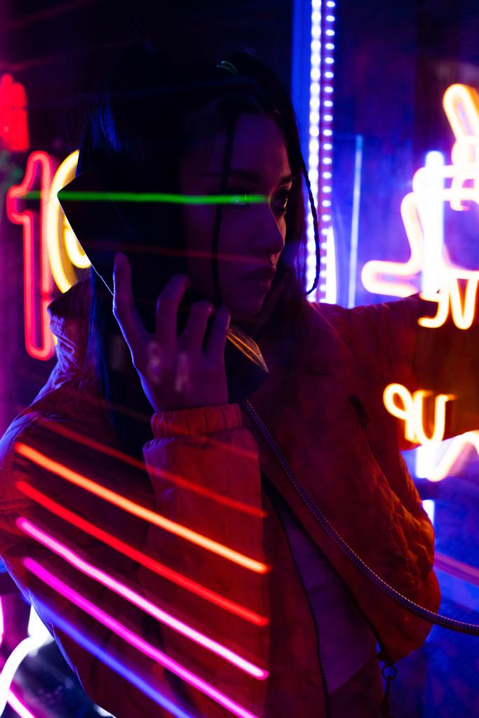 neon lighting on young asian woman talking on retro payphone outside  - Foto, Imagen