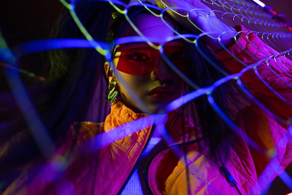 young asian woman in sunglasses looking at camera through metallic fence  - Foto, immagini
