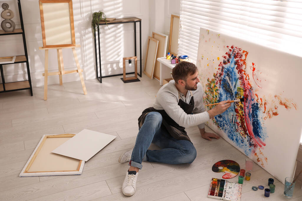 Junger Mann malt im Künstleratelier mit Pinsel auf Leinwand - Foto, Bild