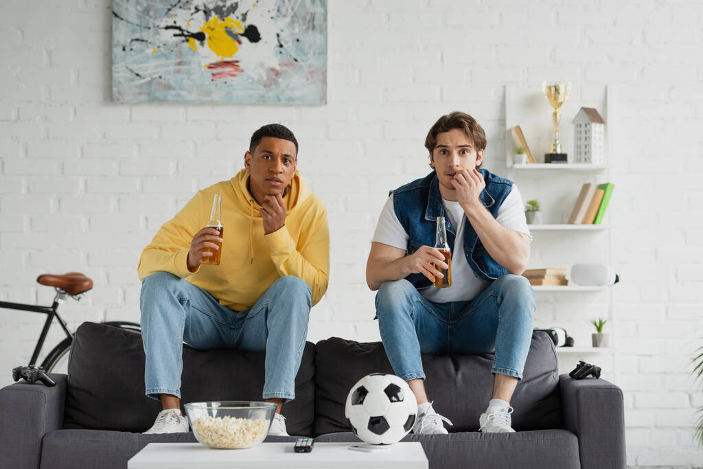 QUIIV, UCRÂNIA - MARÇO 22, 2021: amigos inter-raciais assistindo jogo de futebol com garrafas de cerveja e pipocas na sala de estar - Foto, Imagem