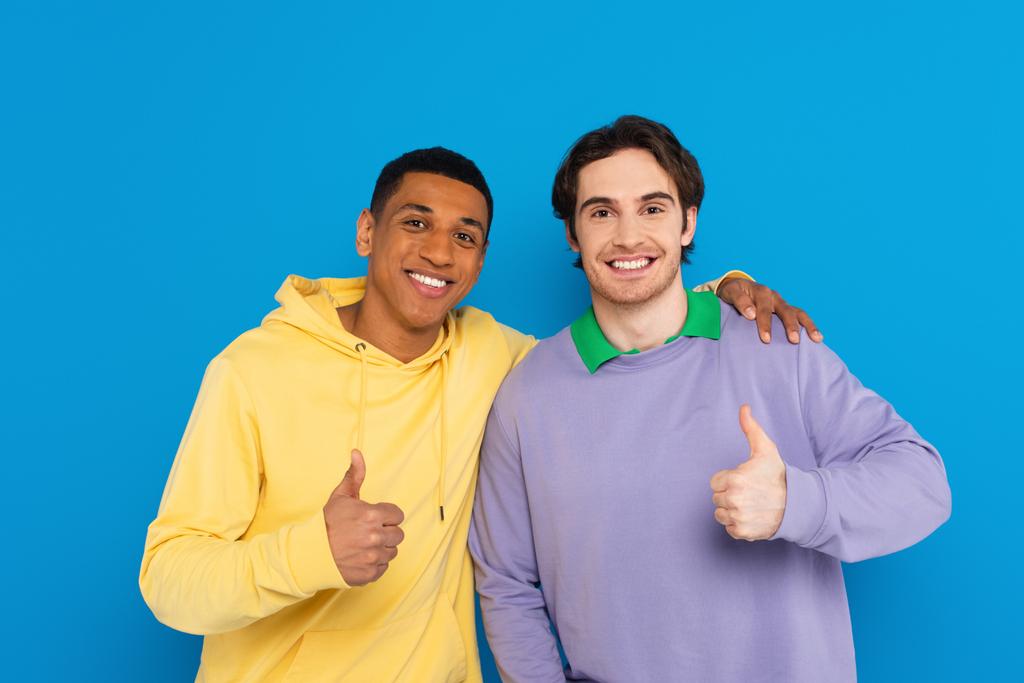 χαμογελαστοί διαφυλετικοί φίλοι που δείχνουν σημάδια απομονωμένα στο μπλε - Φωτογραφία, εικόνα