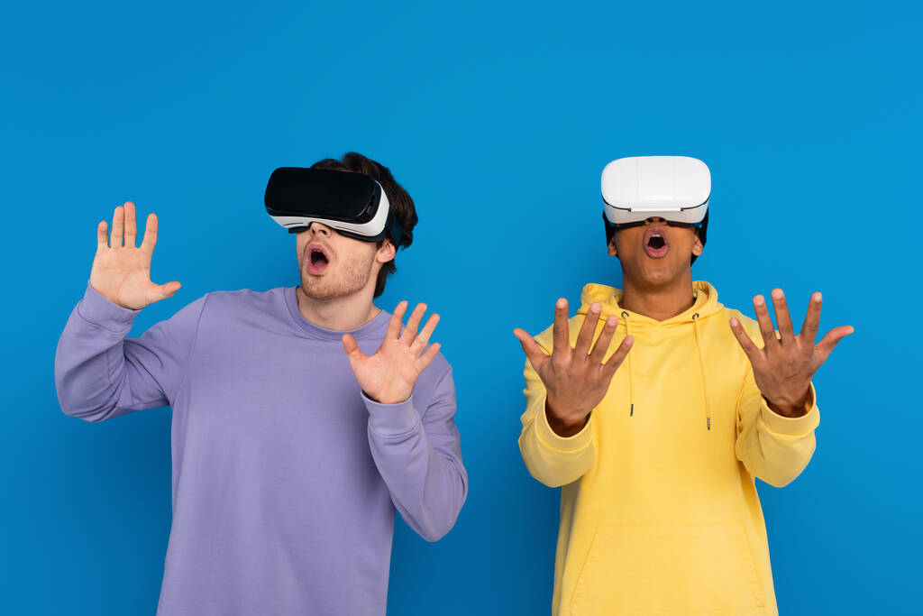 interracial hipsters playing simulation game with virtual reality headsets isolated on blue - Photo, Image