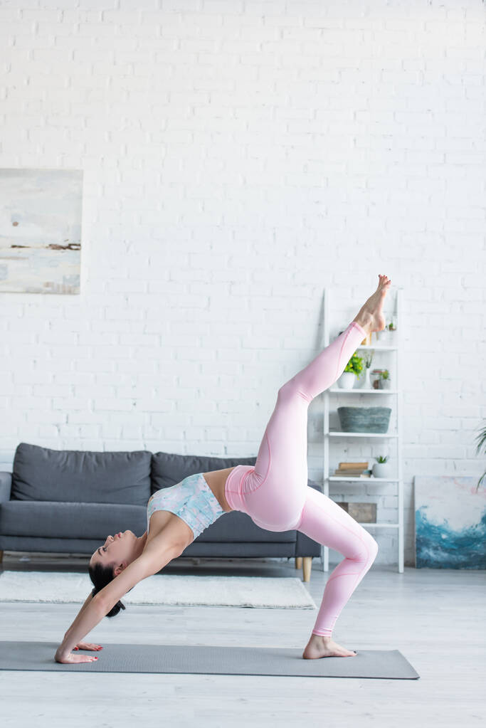 Seitenansicht einer jungen Frau in Sportkleidung, die Yoga in einbeiniger Radpose praktiziert - Foto, Bild