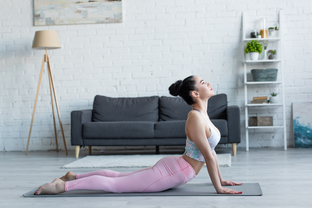vista laterale della giovane donna bruna che pratica yoga in posa alta cobra - Foto, immagini