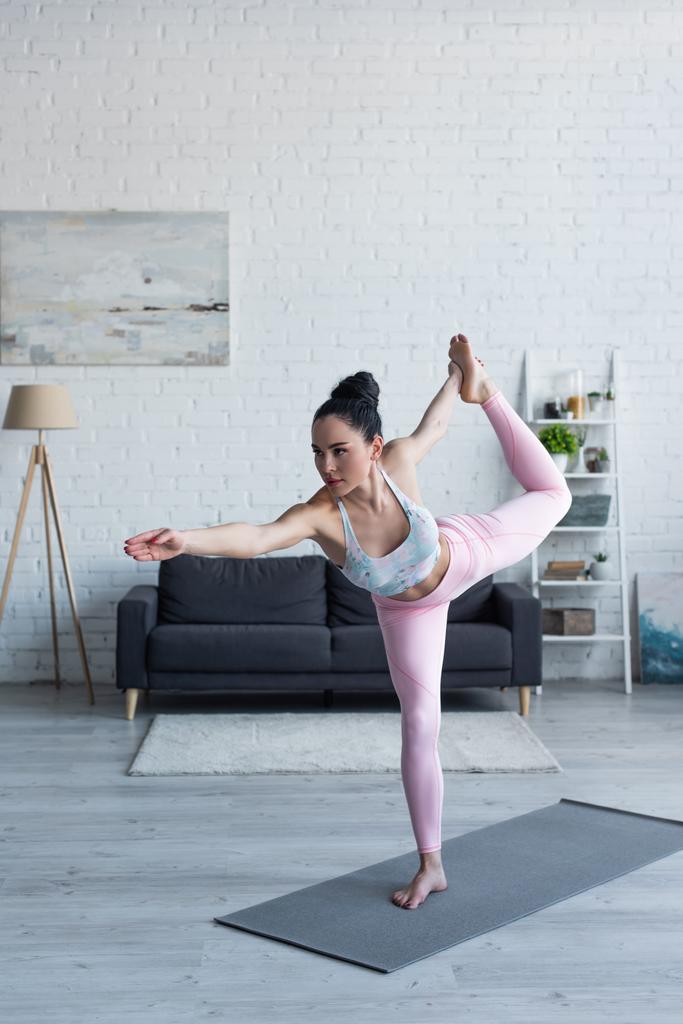 brunette vrouw staande in lord of dance pose tijdens het beoefenen van yoga thuis - Foto, afbeelding