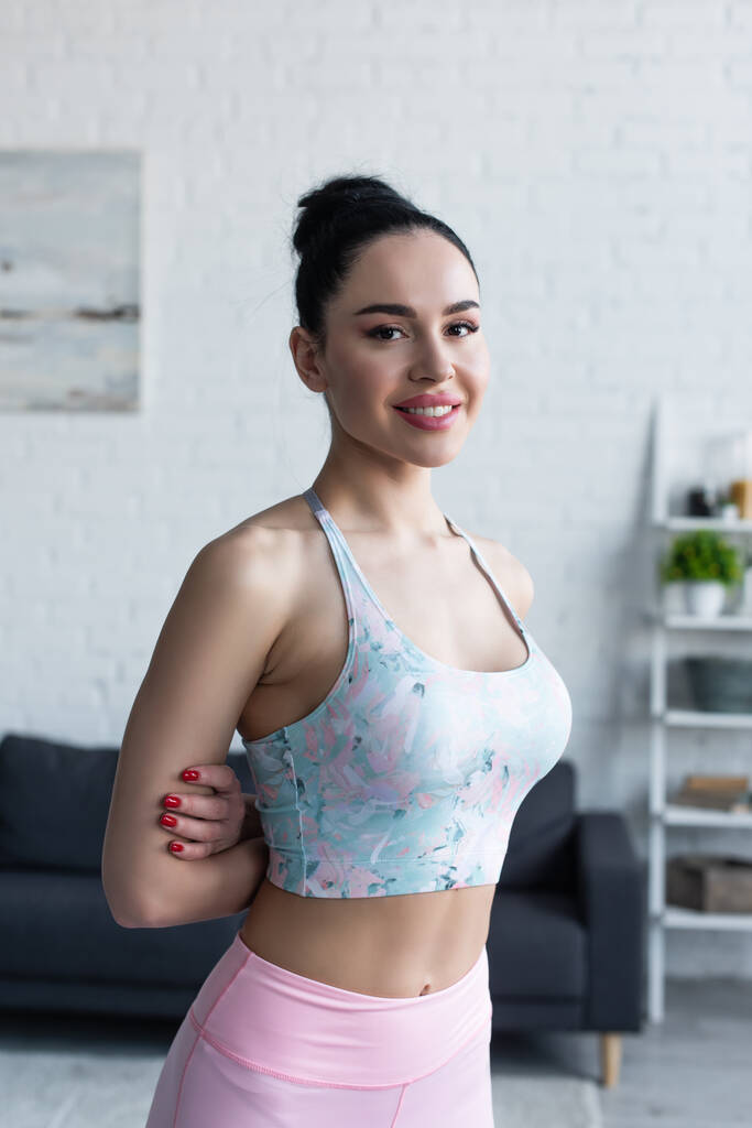 pretty woman in sports bra smiling at camera while standing with hands behind back - Photo, Image