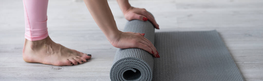 vista recortada de mujer descalza desenrollando estera de yoga en el suelo, pancarta - Foto, Imagen
