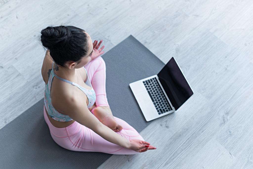 felső nézet a nő meditál lótuszban póz jóga szőnyeg közelében laptop  - Fotó, kép