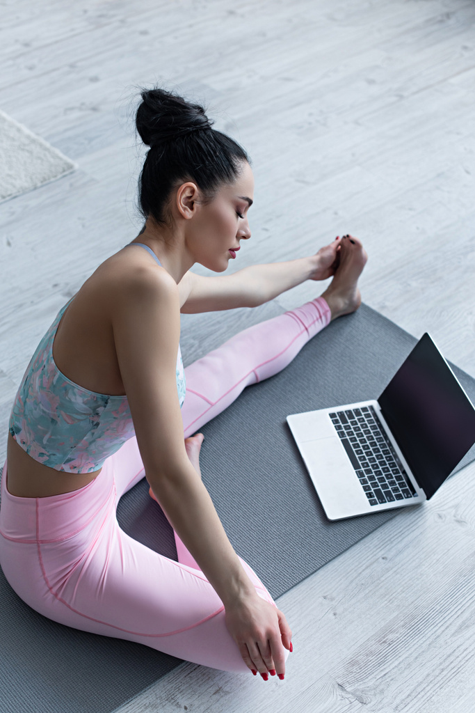 Yoga yaparken dizüstü bilgisayarın yanında boş ekranla poz veren sportif kadın. - Fotoğraf, Görsel
